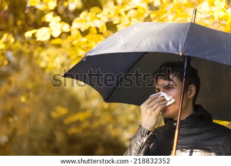 Sick man holding umbrella  and  blowing nose at autumn day