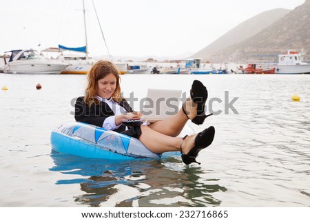 Smiling businesswoman floating in ocean and working on laptop