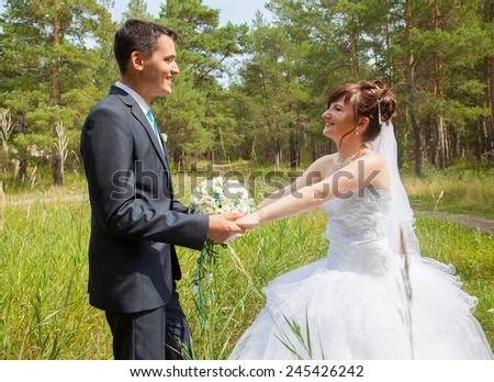 Young groom and bride holding by hands in natural environment while wedding