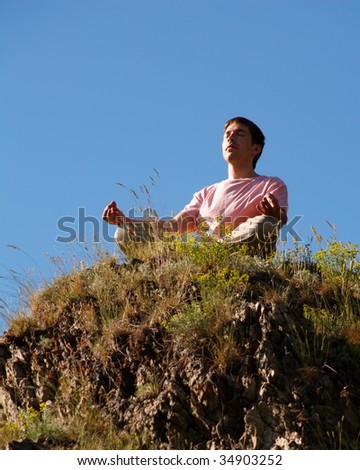 Image of relaxed young man sitting on cliff and meditating outside
