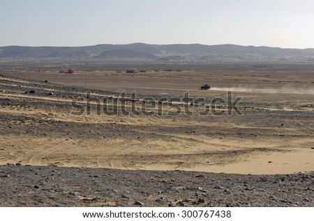 Egypt, Black Desert. Moving off-road vehicle with a panoramic view on the desert hills. Tracks on the sand from the automotive rubber.