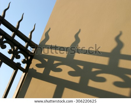 Shadow of metallic fence on the light-coloured walls on background blue sky. Soft focus. Figure Light. Figured forging.