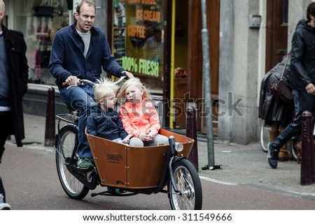 AMSTERDAM, NETHERLANDS - MAY 9: Father with two children  riding bicycles in historical part in Amsterdam, Netherlands on May 9, 2015