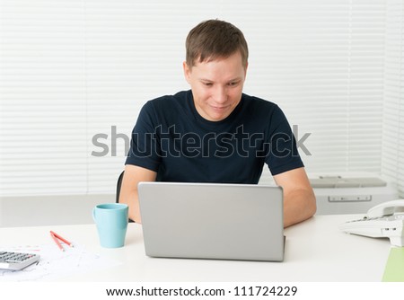 smiling young man sitting at a desk and working on his laptop