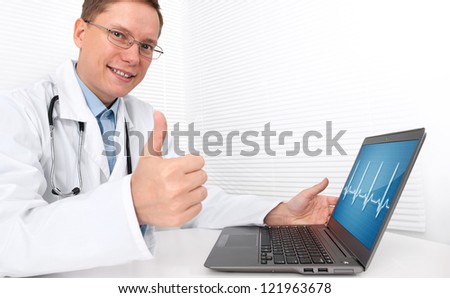 Doctor with laptop sitting in doctor\'s office and showing his thumb up