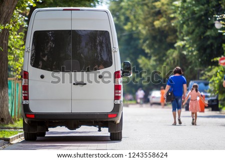 Back view of white passenger medium size commercial luxury minibus van parked n shadow of green tree on summer city street i with blurred silhouettes of pedestrians and cars under green trees. Stock fotó © 