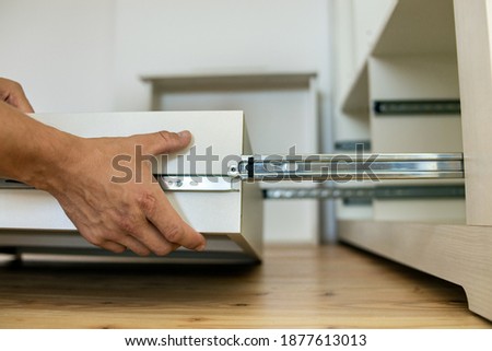 Close up of carpenter hands installing wooden drawer on sliding skids in contemporary cupboard cabinet. Сток-фото © 