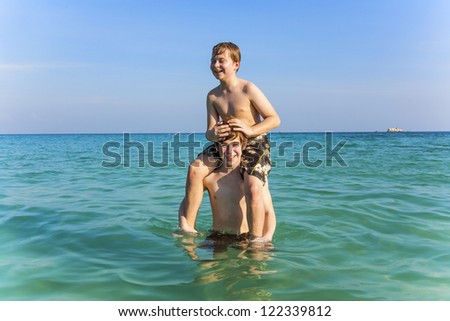 brothers are enjoying the clear warm water at the beautiful beach and playing pickaback