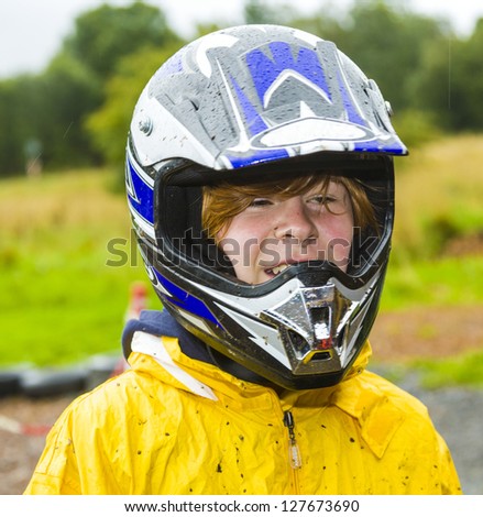 happy boy with helmet at the kart trail in rain with dirty face and clothing