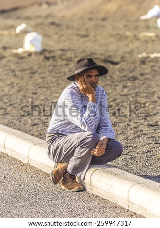 YAIZA, SPAIN - NOV 15, 2014: local camel riding man sits down and waits for tourists in Yaiza, Spain. Camel riding in Timanfaya national park is a must for tourists in Lanzarote.