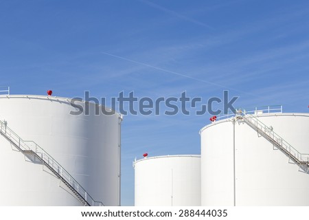 white tanks in tank farm with iron staircase under blue sky