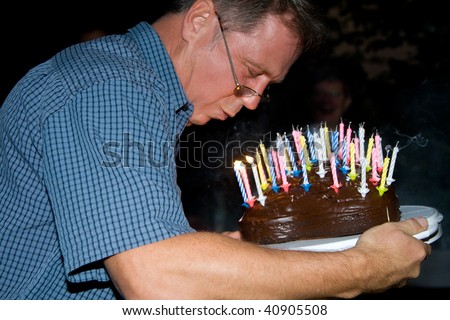 man blows out his birthday candles at the birthday