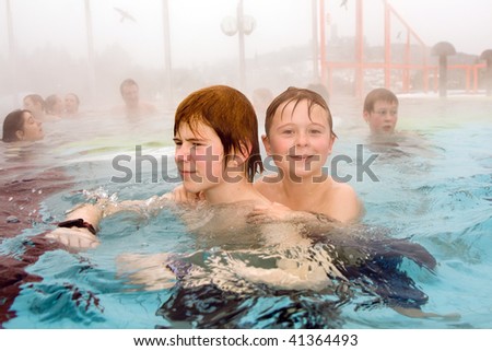 brothers are swimming in the outside area of a thermic pool in Wintertime in warm water, it is foggy