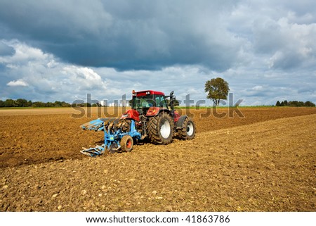 tractor by plowing the acre under cloudy sky with some sun passing by, wonderful landscape