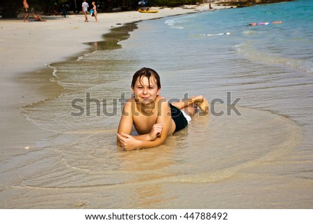 young boy is lying at the beach and enjoying the warmness of the water and looking self confident and happy