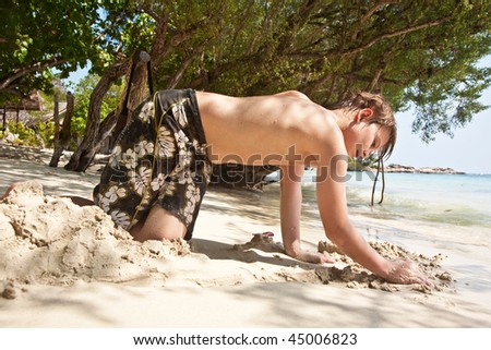 happy young boy is digging in the sand of the beach and constructing sand buildings