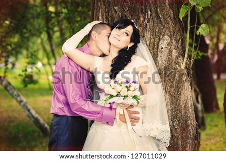 Happy kiss bride and groom near tree on wedding walk. wedding dress. Bridal wedding bouquet of flowers