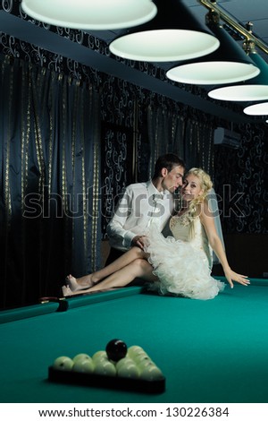 Happy young bride and groom playing billiard at night on their wedding day. Young newlyweds playing billiards at their mansion. Wedding couple. wedding dress. Bridal wedding bouquet of flowers