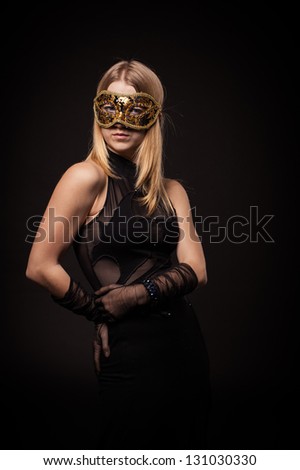 Attractive woman with black masquerade mask, isolated on black. blonde girl in a black evening dress on a black background. Fashion photo of young lady in elegant evening dress.