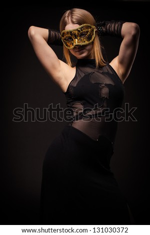 Attractive woman with black masquerade mask, isolated on black. blonde girl in a black evening dress on a black background. Fashion photo of young lady in elegant evening dress.