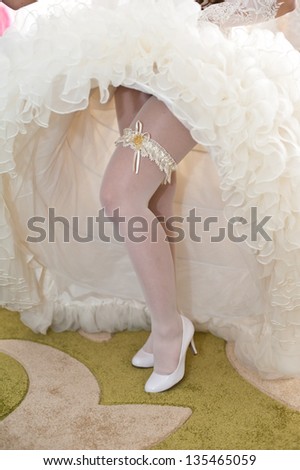 Beautiful leg of the young bride. Garter on the leg of a bride, slim sexy bride in wedding luxury dress showing her silk garter with golden ribbon. woman have a final preparation for wedding ceremony