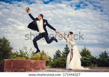 Groom jump up and fly away. Happy young bride and groom outside on their wedding day - Copy space. Wedding couple - new family! wedding dress. wedding bouquet of flowers