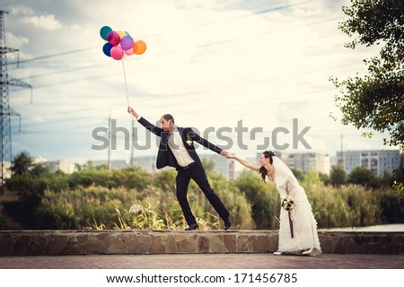 Groom flies on the balloons, but the bride holds his hand. Funny wedding. Groom jumps and flies on balloons. Young husband flying from his wife. Funny wedding concept. Happy Valentines day!