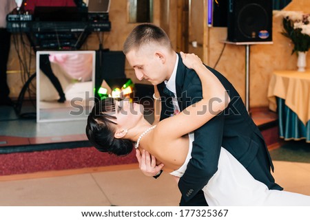 Wedding. Just married couple dancing in front of their unrecognizable friends. Kiss and dance young bride and groom in dark banqueting hall. Happy holiday of new family. Wedding bouquet, bridal dress