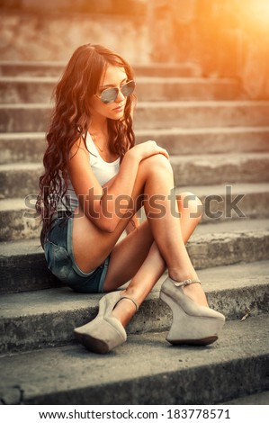 Portrait of a beautiful young woman sitting on stairs outdoors. beautiful young woman smiling. young woman in colorfull summer clothes sit on stairs outdoor shot
