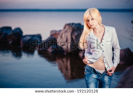 Blonde girl walking barefoot in jeans and a white shirt on the river at sunset. Walk on the water after work
