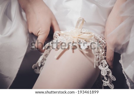 bride dresses garter on the leg. Picture of beautiful female barefoot legs in wedding dress. Bride dresses stockings on feet. Bride putting a wedding garter on her leg