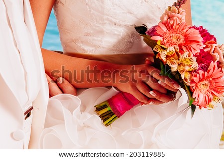 hands of the bride and groom on a beautiful wedding bouquet. Beautiful wedding bouquet in hands of the bride on sea background