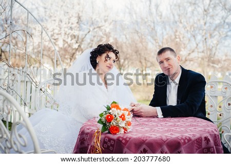 Bride and groom posing at the decorated banquet table in the park in the summer. Hand in hands. Enjoy a moment of happiness and love. A series of photos in my portfolio. Wedding flowers on a table