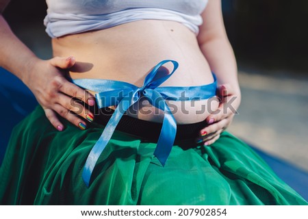 Pregnant girl sitting on a boat on the river bank. Belly of a pregnant woman on the nature. Beautiful belly of young attractive pregnant woman walking outdoor