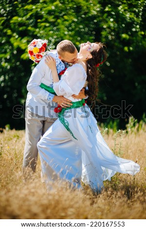 Ukraine. Happy ukrainian wedding (bridal) couple in the ukrainian style. Beautiful bride and groom in the ukrainian style are standing with bouquet. Female and male models. . park summer outdoor