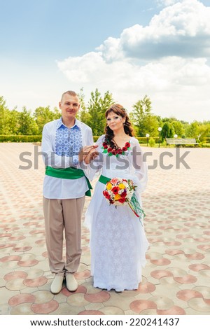 Ukraine. Happy ukrainian wedding (bridal) couple in the ukrainian style. Beautiful bride and groom in the ukrainian style are standing with bouquet. Female and male models. Indoors, close up.