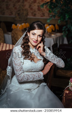Gorgeous bride blonde in wedding dress in luxury interior with diamond jewelry posing at home and waiting for groom. Romantic rich brunette bride in a luxurious wedding dress in expensive interior