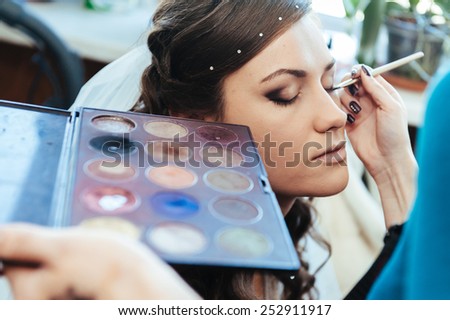 Woman applying make up for a bride in her wedding day near mirror. Closeup of a makeup artist applying makeup