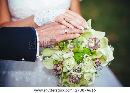 Bride and groom\'s hands with wedding rings near wedding bouquet