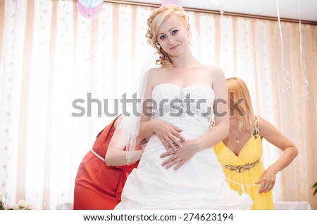 Bridesmaid is helping the bride to dress. Friends helping bride get into dress