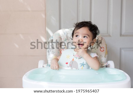 Similar – Image, Stock Photo Baby seated in high chair reaching for spoon; dramatic natural lighting and messy tray table