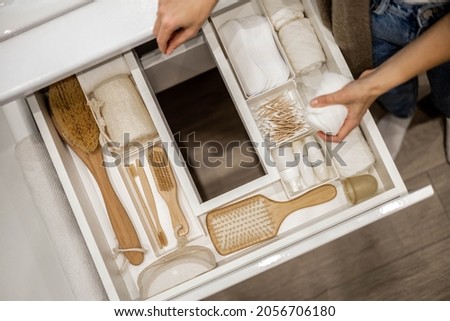 woman is holding wooden brush and putting into the drawer together with bathroom amenities. Housewife is organizing bathroom storage. Konmari method of bathroom declutter. Copy space.
