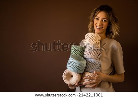 Portrait smiling blonde woman clothes and accessories design holding pile of multicolored hank reel ribbon yarn. Adorable creative female enjoying art handmade work hobby posing isolated on brown Stock fotó © 