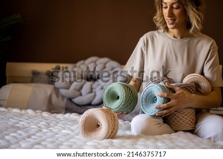 Portrait smiling blonde woman clothes and accessories design holding pile of multicolored hank reel ribbon yarn. Adorable creative female enjoying art handmade work hobby posing isolated on brown Stock fotó © 