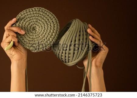 Closeup female hands holding hank of green ribbon yarn and knitting decor or clothes isolated on brown background. Woman arms enjoying art work or hobby creating handmade accessories Stock fotó © 