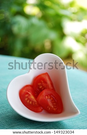 Red tomatoes salad in heart shape bowl on green natural background