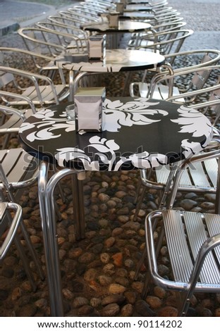 Row of metal chairs and black and white tables in an outdoor bar