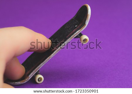 Small skateboard on purple background. fingers on tiny skate. playing with fingerboard. home leisure concept. copy space 商業照片 © 