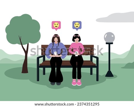 Two young girls with light skin of European appearance in fashionable clothes are sitting on smartphones in the park on a bench next to a tree and a lantern. They send each other emoticons