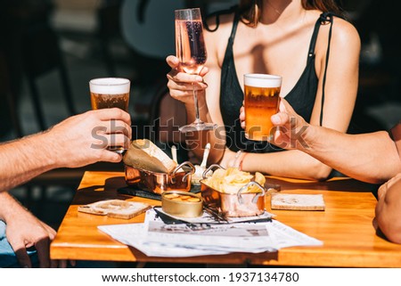 Group of friends sitting on a summer terrace with beer and wine in their hands and snacks on the table
